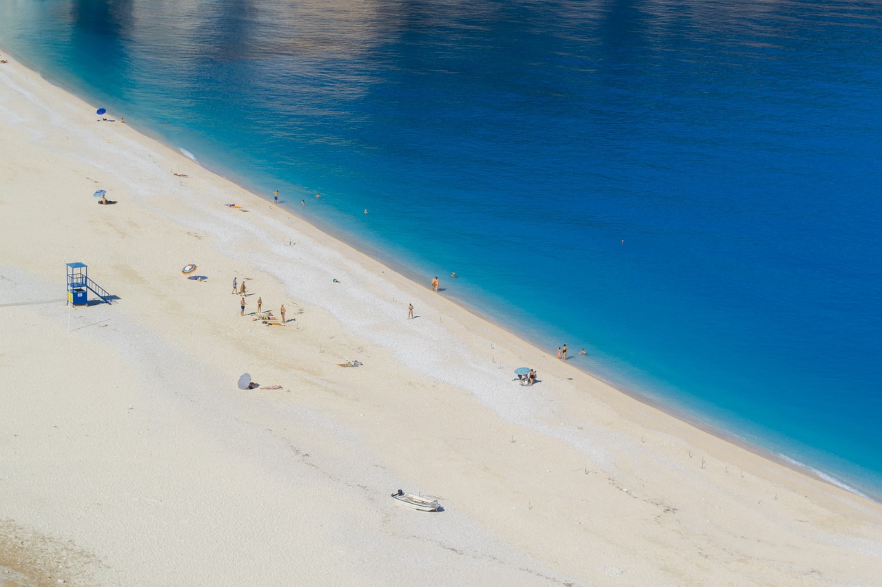 Spiaggia affollata con molte persone sotto il sole, ombrelloni colorati e mare blu.