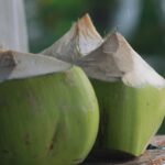 Acqua di cocco versata in un bicchiere con cocco fresco sullo sfondo.