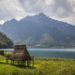 Vista panoramica del lago che ricorda un fiordo, circondato da montagne e vegetazione verdeggiante.