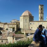 Anziani seduti su panchine nella piazza di un borgo toscano, mentre raccontano storie del passato.