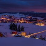 Panorama di una località alpina innevata, con chalet e figuranti in costume natalizio.