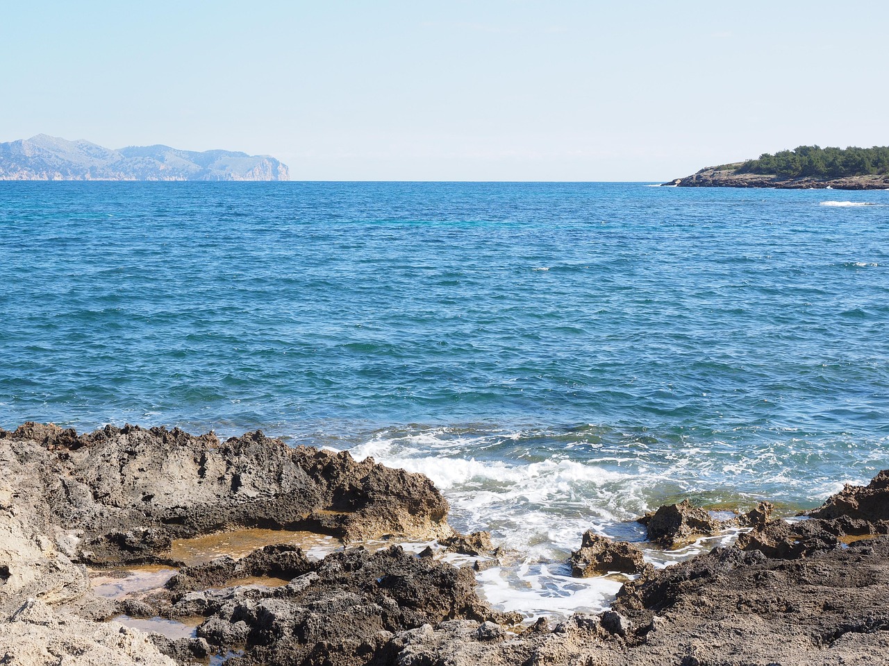 Spiaggia di Maiorca affollata con sabbia dorata e mare cristallino sotto un cielo azzurro.