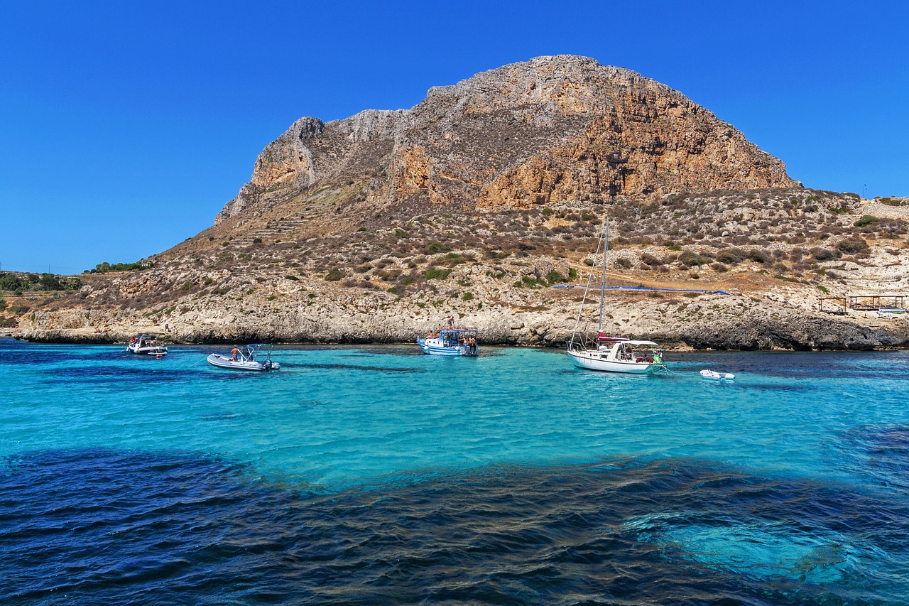 Panorama di Lampedusa con il mare cristallino e la costa rocciosa, simbolo di bellezza e sfide migratorie.